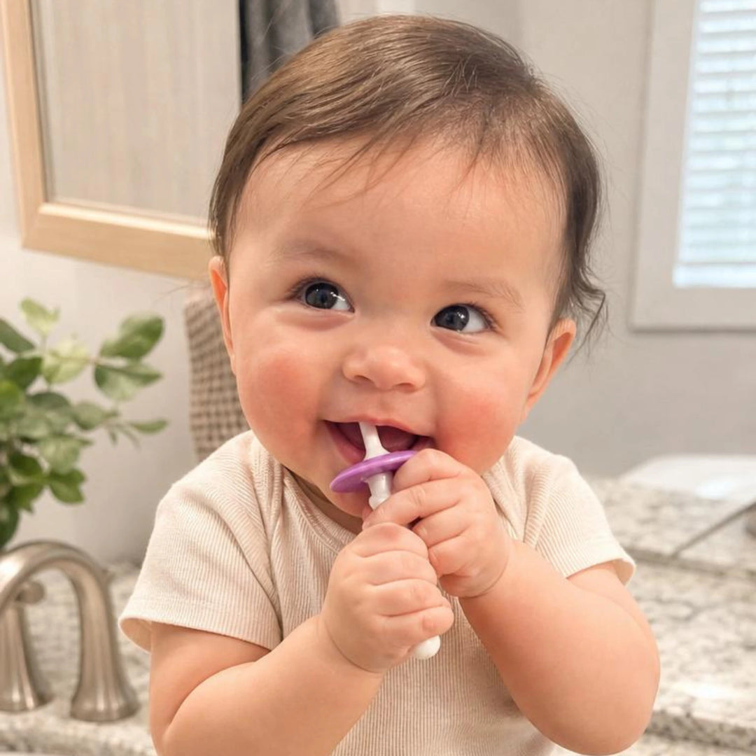 Un bébé tient sa brosse Dandelion Bébé en bouche, dans une salle de bains