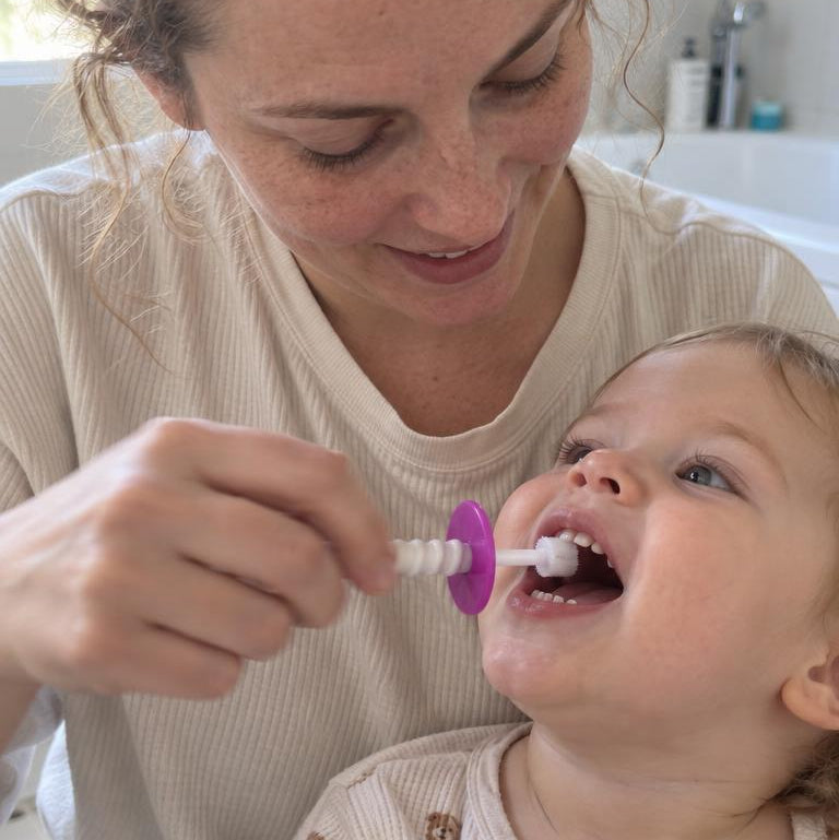 Une maman brosse les dents de son enfant avec la brosse Dandelion Bébé